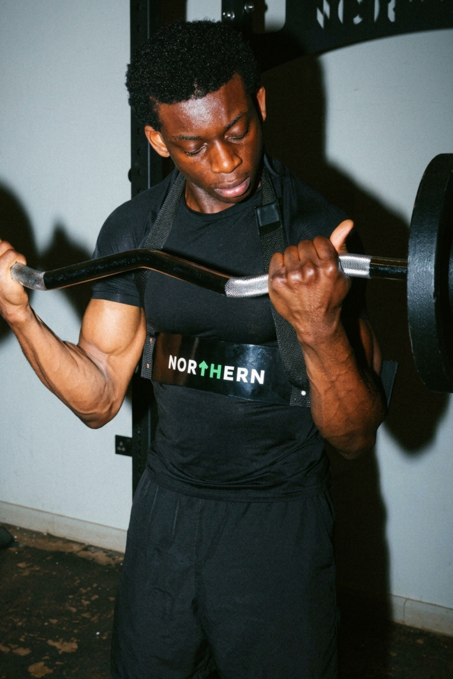 Man performing barbell curl using EZ bar loaded with cast iron weight plates in home gym